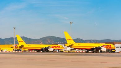Yellow DHL freighter jets sit by the DHL terminal at an airport on a sunny day.