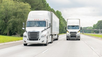 a pair of white tractors pulling trailers on a highway