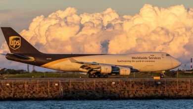 Side view of a brown-tail UPS 747 jumbo jet with setting sun conditions and white clouds in background.