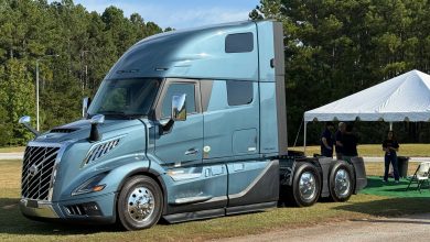 A blue Volvo VNL semi-truck on display at an outdoor event at the Michelin Laurens Proving Grounds, with people gathered under a tent in a forested setting.