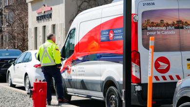 A driver wearing a yellow vest prepares to step into a Canada Post van on a city street.