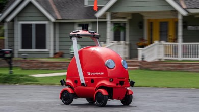 A red delivery robot on wheels rolls down a neighborhood street.