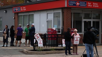 Canadian Union of Postal Workers members are on strike carrying placards outside a post office.