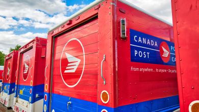 Rear view of red/blue Canada Post vans lined up in parking lot.