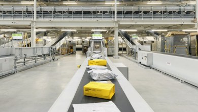Yellow packages move on a conveyor belt at a large shipping center.