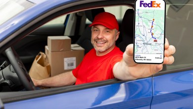 Image of a courier reaching out of car window with phone showing a FedEx app.