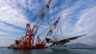 A barge with a heavy crane lifts a broken aircraft section from the sea after an accident.