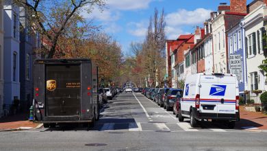 UPS and USPS vans are parked on opposite sides of a city street, seen from the rear.
