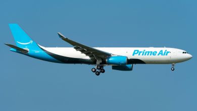A light-blue tailed Prime Air freighter, controlled by Amazon, is seen on approach with its wheels down against a blue sky.