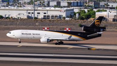 A brown-tailed UPS cargo jet lands on a runway on a sunny day.