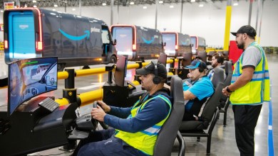 Amazon drivers wearing yellow vests sit in front of large training simulators.