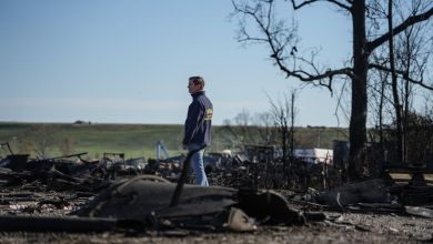 A man walks around charred wreckage from a big fire.
