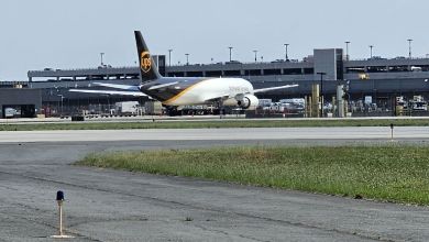 A brown-tailed UPS freighter aircraft is parked at an airport terminal on a sunny day.