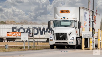 A Yellow truck exiting a gate with a Roadway trailer in the background
