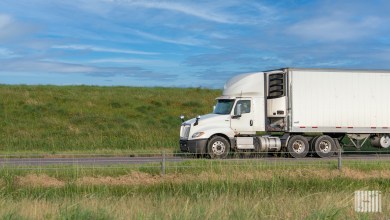 a white tractor pulling a refrigerated trailer on a highway