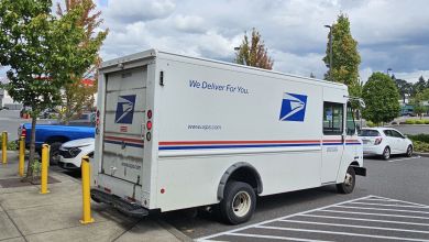 Side-rear view of a USPS package van parked in a strip mall lot.