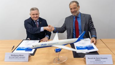 Two men shake hands at a desk with a model airplane that says Silk Way West Airlines to complete an aircraft purchase transaction.
