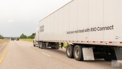 A white RXO trailer being pulled by a white sleeper cab on a highway