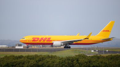A yellow plane with red DHL lettering seen from side taxiing at an airport.