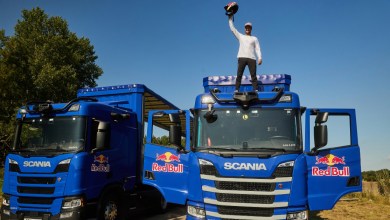 Red Bull athlete Matt Jones celebrates on top of a Scania autonomous truck, raising his helmet in triumph after becoming the first person to jump between two moving self-driving Scania trucks