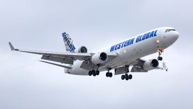 A tri-engine Western Global freighter with wheels down approaches an airport as seen from below on an overcast day.