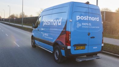 Rear view of a light blue PostNord delivery van driving down the highway.