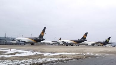 Three brown-tailed UPS jets are parked at an airport terminal with some snow on the ground.