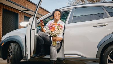 A woman driver gets out door holding a vase of flowers.