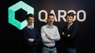 Three Qargo co-founders, Adriaan Coppens (center), pose confidently in front of the company's illuminated hexagonal logo, highlighting their AI-driven TMS growth after $33 million Series B funding.
