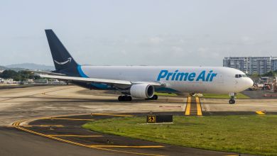 An Amazon Prime Air cargo jet with a dark blue tail moves on an airfield under sunny conditions.