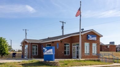 A small brick post office with a U.S. flag flying on a sunny day.