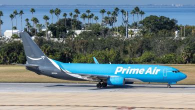 A two-toned blue Amazon Prime Air jet taxis on the runway at Tampa International Airport with palm trees in the background.
