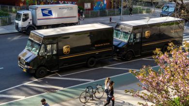 Two UPS trucks are parked back-to-back along a street curb and a larger USPS truck is parked on the other side of the street.