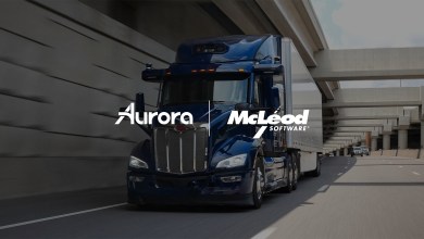 Blue Peterbilt semi-truck on highway with Aurora Innovation and McLeod Software partnership branding for autonomous trucking TMS integration