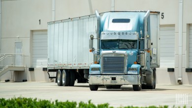 a blue tractor backing a trailer up to a warehouse dock door