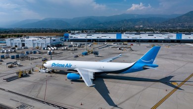 A large Amazon Prime Air cargo jet with light-blue tail seen on the tarmac, seen from the side and looking down.