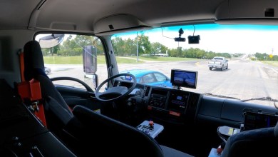 Interior of a Gatik fully driverless medium-duty autonomous truck cab, showing an empty driver’s seat, dashboard with monitoring screens, and forward view of the road during revenue-generating commercial delivery operations in North America.