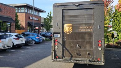 Rear view of a brown UPS van in a strip mall parking lot.