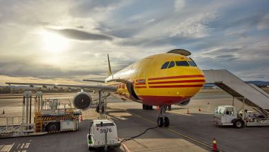 Front view of a mustard-yellow DHL cargo plane parked at the airport.