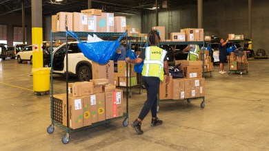 Warehouse worker wearing yellow vest pushes a cart loaded with parcels.