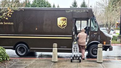 A side view of a brown UPS van with the driver jumping on board on a rainy day.