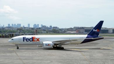 A purple-tailed FedEx plane seen from the side with a city's high-rise buildings in the background.