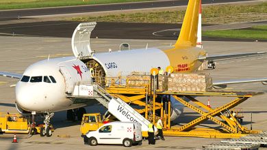 A white-and-yellow freighter aircraft sits on the tarmac with its cargo door open as seen from a raised front position.