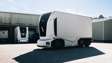 Einride autonomous electric trucks parked in a sunny industrial yard outside a warehouse