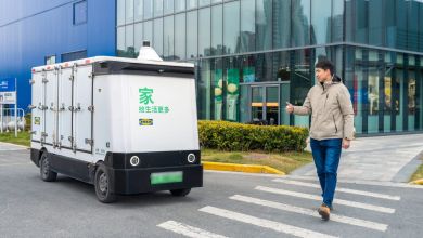 An autonomous delivery van stops at a crosswalk for a male pedestrian.