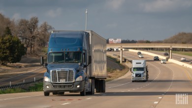 a blue tractor pulling a trailer on a highway