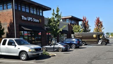 A UPS Store with a UPS van and cars in the parking lot out front.
