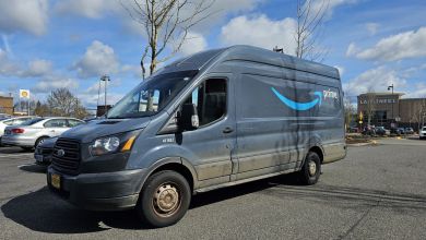 A side view of a blue Amazon delivery van in a shopping center parking lot.