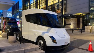 White Tesla Semi electric semi-truck parked at night in an urban plaza next to a traditional black semi-truck, illustrating mixed fleet EV and ICE operations.