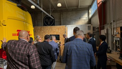 Samsara 2026 North America Customer Advisory Board members gather for an in-person session at an industrial warehouse facility, viewing a demonstration next to a prominent yellow DHL truck.